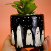 Ceramic pot with ghost design held by a hand against an orange background