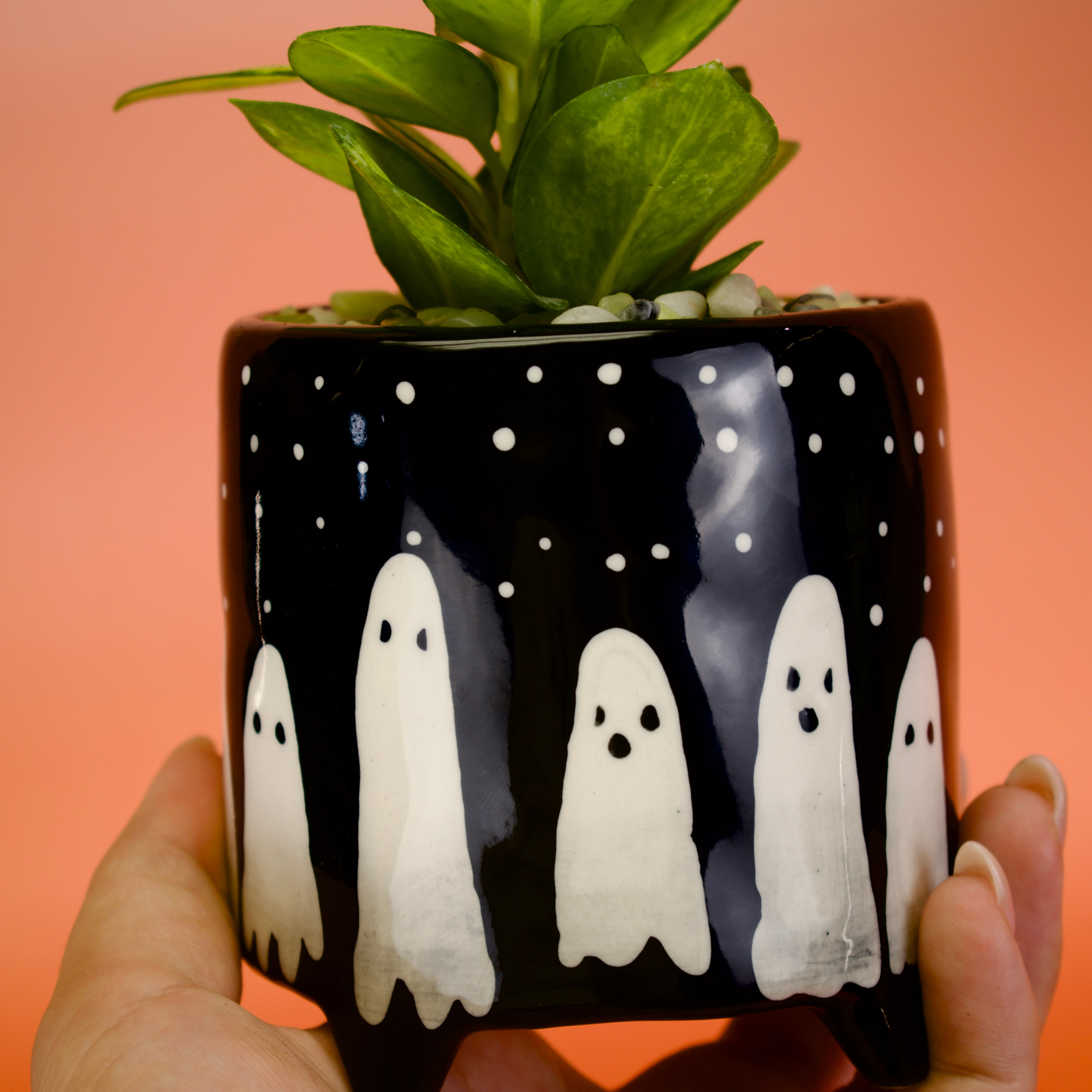 Ceramic pot with ghost design held by a hand against an orange background